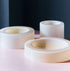 Three smooth cream-white bowls, arranged beautifully on top of a cream pink table, each bowl having different heights and widths, a dark wall in the background. 