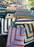 Collection of colorful patterned pillows on a dark surface with a window and plant in the background.