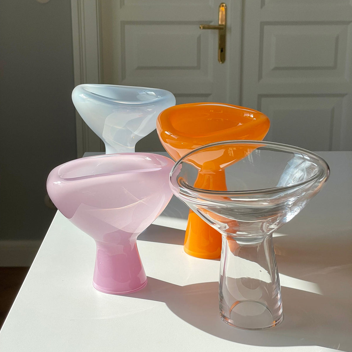 Four colorful glass bowls on a white surface with a door in the background