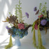 Two floral arrangements in light blue phantom dishes acting as vases on a white surface with a white background
